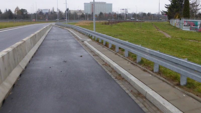 Never used merging lane blocked by a concrete barrier. Necessary infrastructure for pedestrians and cyclist was not provided, so they have to use the muddy path on the right side.